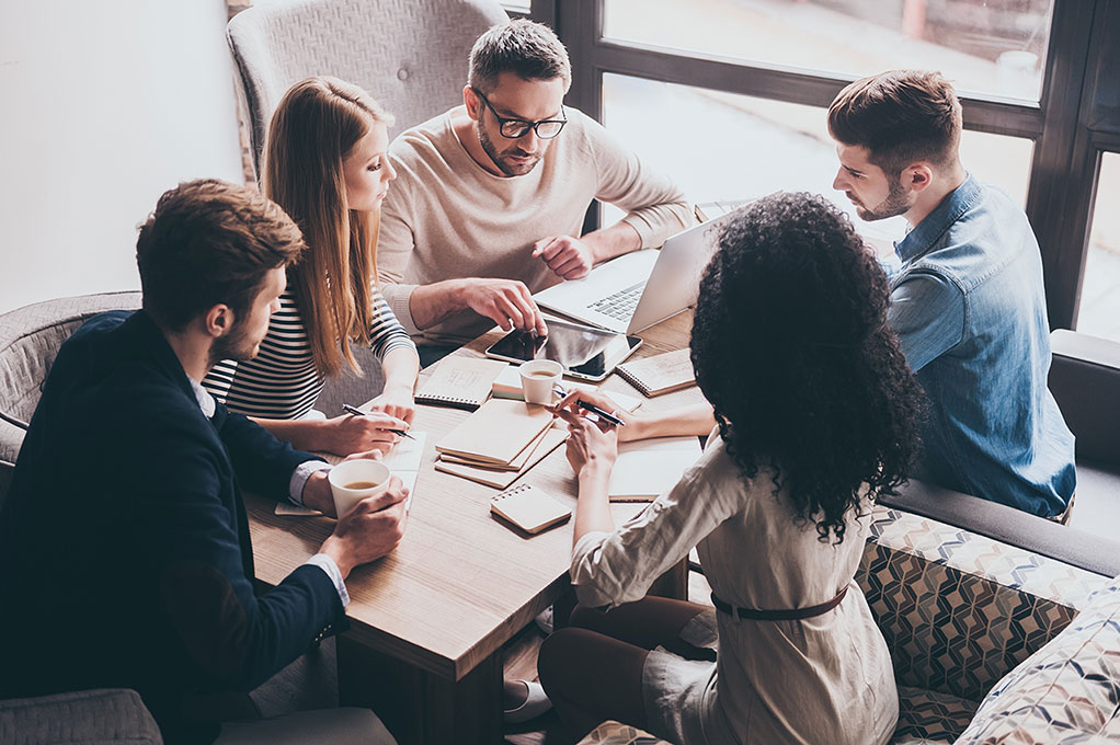 Personen sitzen um Tisch herum und arbeiten