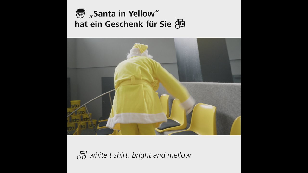 Szene aus dem STO-Weihnachtsvideo Santa in Yellow: ein Weihnachtsmann im Sto-Gelb geht durch das Firmengebäude an gelben Sto-Eimern vorbei