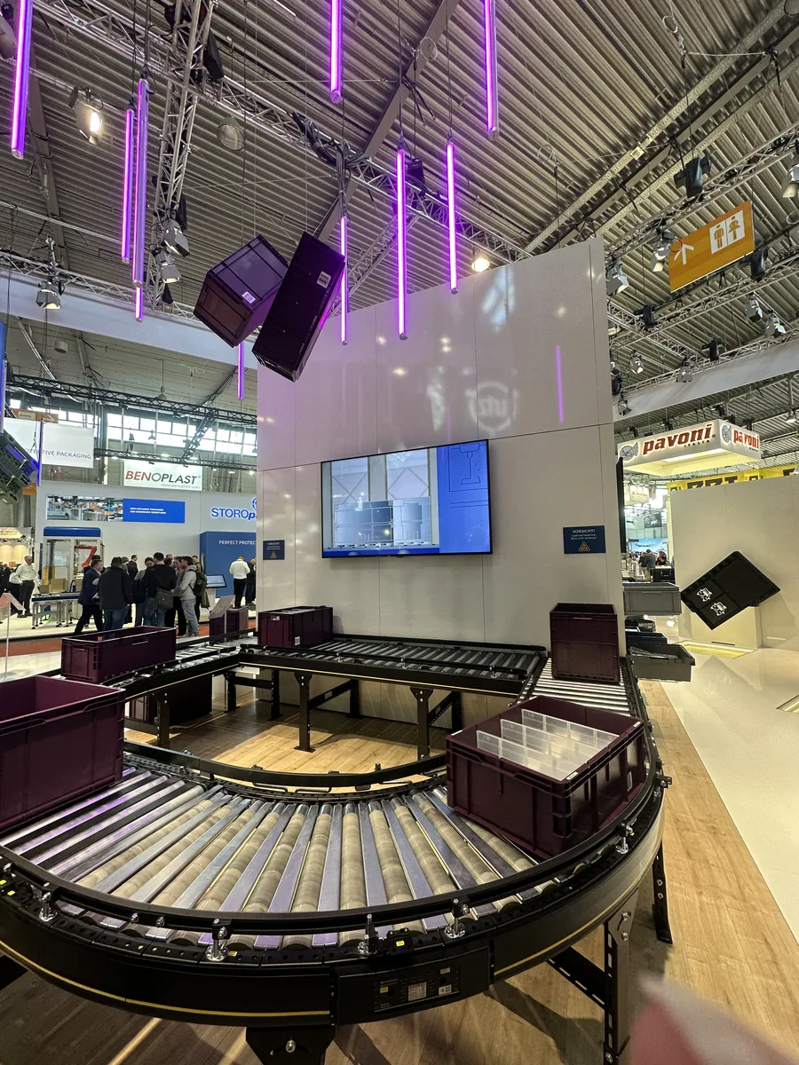 Messestand von Georg Utz auf der LogiMAT 2026 mit Förderstrecke, Mehrwegbehältern und Bildschirm für das Standvideo