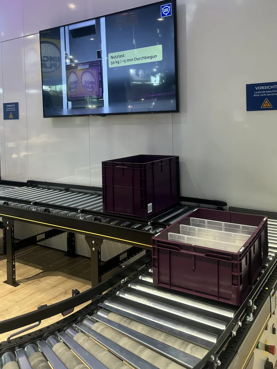 Bildschirm am Georg-Utz-Stand auf der LogiMAT über der Rollenbahn mit Logistikbehältern